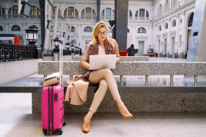 Woman Uses Laptop Waiting with Luggage